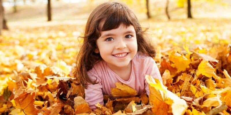 little girl smiling in a pile of leaves