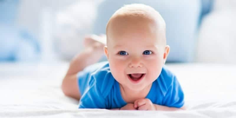 baby laughing in blue onesie on bed