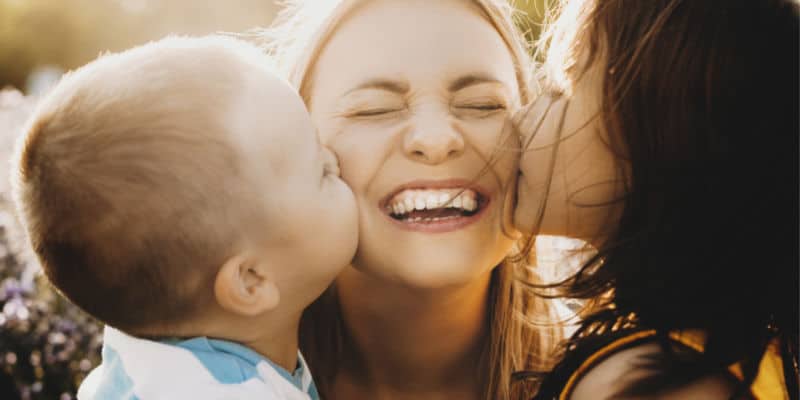 toddler and older daughter kissing a mother's cheek on mother's day