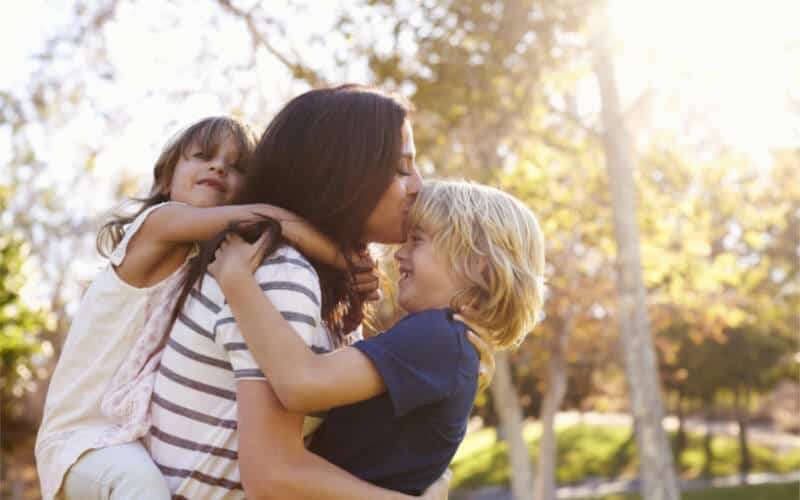 mother kissing two siblings outside