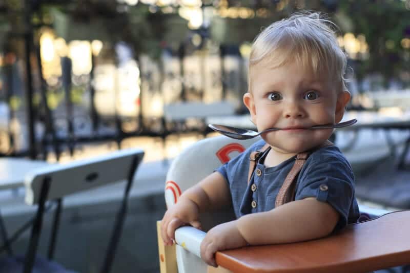 adorable baby in highchair with spoon in his mouth