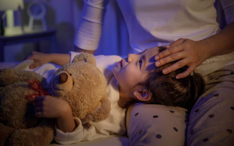 mom putting son to bed at bedtime with teddy bear