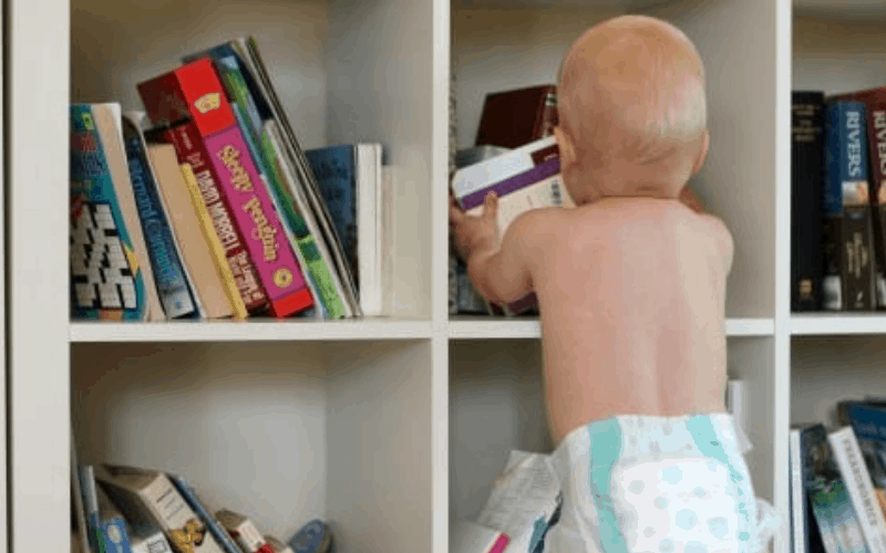 Baby uses organization with kids on book shelf. 