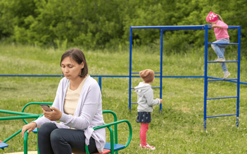 Mom is being selfish by scrolling on her cell phone while kids are playing. 